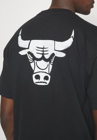 Camiseta de algodón negra con un gran gráfico de toro blanco en la parte posterior. Diseño de manga corta y cuello redondo, textura suave.