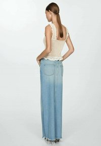 Top in maglia all'uncinetto di colore crema con bordi in pizzo; abbinato a una lunga gonna di jeans blu chiaro con sfumature, caratterizzata da orlo strappato e tasche posteriori.