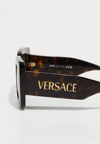 Kvadrāta formas saulesbrilles ar bruņurupuča apdari un zelta toņa "VERSACE" logo uz templīša. Gluda faktūra, spīdīga apdare.