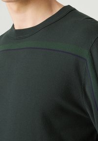 Pull en laine à col rond de couleur vert foncé avec des rayures contrastantes vertes et violettes sur la poitrine. Tissu doux avec une texture lisse, design ajusté.