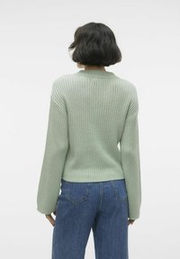 Pulover verde deschis, cu dungi, cu un gât rotund și mâneci lungi, asortat cu blugi blue denim cu talie înaltă, evidențiind o siluetă ajustată.