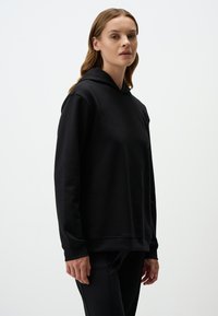 Czarna bluza z kapturem w luźnym fasonie, z długimi rękawami i przednią kieszenią typu kangur. Wykonana z gładkiego, miękkiego materiału z regulowanym kapturem.