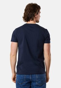 Navyblaue Baumwoll-T-Shirt mit kurzen Ärmeln, rundem Ausschnitt und schlichter Gestaltung. Getragen mit blauen Jeans, die eine lockere Passform von hinten zeigen.