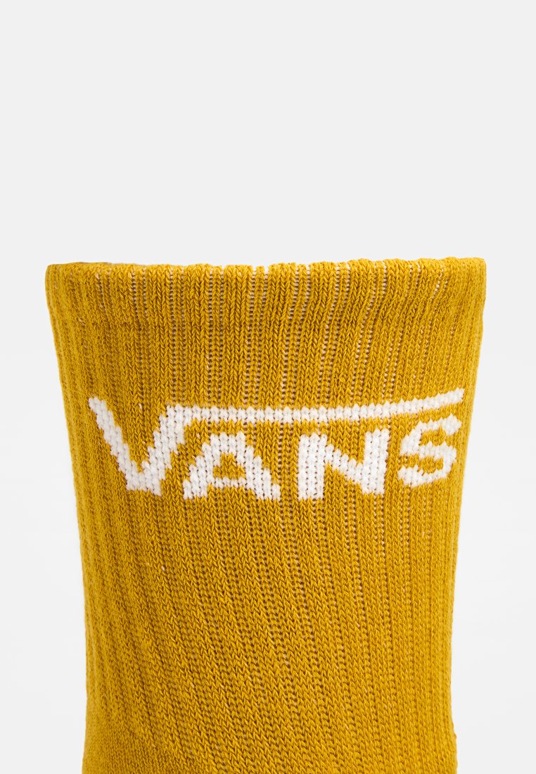Cuff di calza a coste gialle con logo Vans bianco centrato vicino alla parte superiore su uno sfondo chiaro e uniforme.