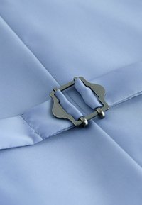 Gros plan sur une boucle métallique attachant une ceinture en tissu bleu clair sur un textile lisse bleu clair.