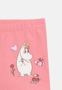 Λευκό καρτούν ιπποπόταμος με ξανθά μαλλιά στέκεται κοντά σε κόκκινα τριαντάφυλλα, ένα ροζ δώρο με κόκκινο φιόγκο και μια ροζ καρδιά σε ροζ υφασμάτινο φόντο.