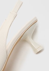 Sapato de salto slingback branco com parte superior texturizada, salto de plástico alargado e sola lisa, apresentando um design minimalista e linhas limpas.