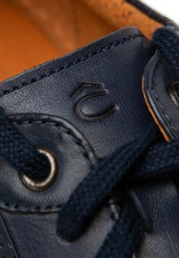 Granatowe skórzane sneakersy z teksturowaną powierzchnią, kontrastującym brązowym wnętrzem oraz ciemnymi sznurowadłami z metalowymi oczkami. Widoczny szczegół wytłoczonego logo.