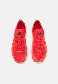 Røde Nike Free-sko med mesh-overdel, teksturert design, flate lisse og svarte logo-detaljer. Hvit gummisåle, lett konstruksjon.