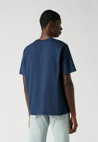 Camiseta de algodón azul marino con mangas cortas y escote redondo. La parte trasera es lisa, y presenta un corte relajado y una textura suave.