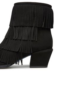 Schwarze Wildleder-Stiefeletten mit geschichtetem Fransen-Detail, Blockabsatz und runder Spitze. Die Textur ist weich und plüschig, was den Reichtum des Materials betont.