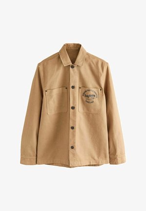 Brązowa kurtka robocza wykonana z bawełny. Posiada zapięcie na guziki z przodu, dwie kieszenie na piersi oraz nadrukowane logo z tekstem na lewej kieszeni.