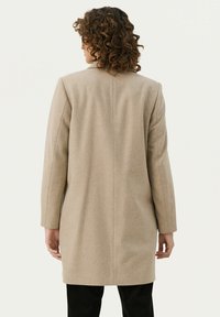 Beige Wollmantel mit taillierter Silhouette, einem Schlitz auf der Rückseite und langen Ärmeln. Glatte Textur und minimalistische Designmerkmale.