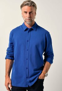 Modrá košile s dlouhým rukávem a límečkem, s fialovými knoflíky, hladkou texturou a ohrnutými rukávy. Nosit s tmavými džíny.