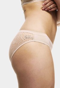 Panty in un morbido colore nude, realizzato in un mix di pizzo e tessuto, con accenti in pizzo floreale sui lati, texture liscia e design a vita bassa.