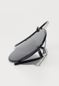 Ochelari de soare ovali negri cu lentile întunecate, brațe metalice elegante și un design minimalist. Temele subțiri notabile amplifică aspectul ușor.