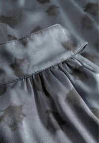 Grauer Stoff mit einer weichen, strukturierten Oberfläche, der dunkle abstrakte Muster und ein gerafftes Taillendetail aufweist.