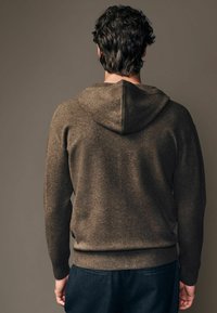 Brązowy, fakturowany hoodie z kapturem na sznurki, z prążkowanymi mankietami i dołem, zestawiony z ciemnymi spodniami, widoczny z tyłu na neutralnym tle.