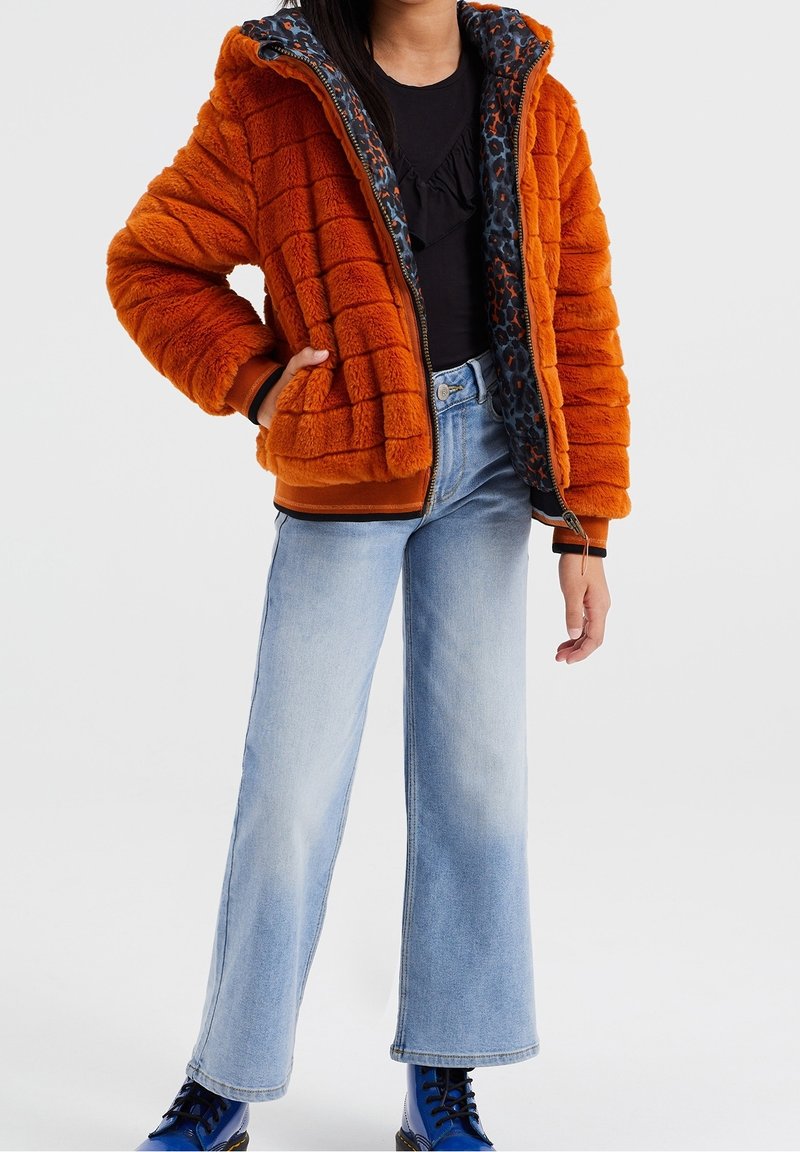 Orange quiltad fuskpälsjacka med huva, med ett leopardmönstrat foder. Matchas med ljusblå utsvängda jeans och blå ankelboots.