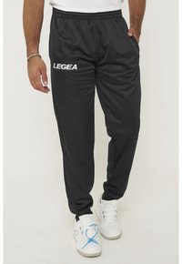 Zwarte sportbroeken met een elastische tailleband, voorzien van zijzakken en het woord "LEGEA" in het wit op het linkerpijpen. Gladde textuur.
