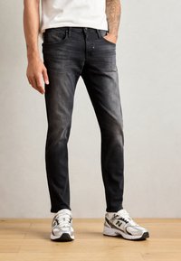 Jeans negri slim-fit, cu un finisaj decolorat, design cu cinci buzunare și detalii de cusătură subtile, asortați cu pantofi sport albi.