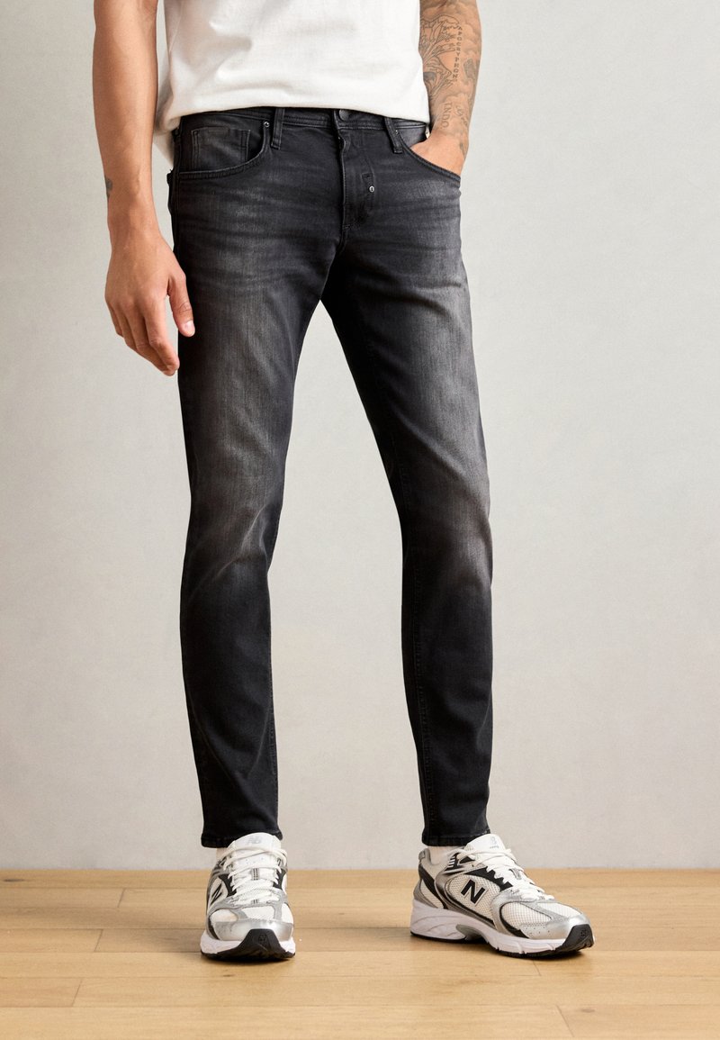 Jeans negri slim-fit, cu un finisaj decolorat, design cu cinci buzunare și detalii de cusătură subtile, asortați cu pantofi sport albi.