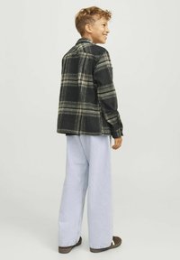 Camisa a cuadros negra y verde, mezcla de lana, corte relajado. Pantalones vaqueros de pierna ancha azul claro, textura suave, combinados con zapatos marrones. Vista trasera.