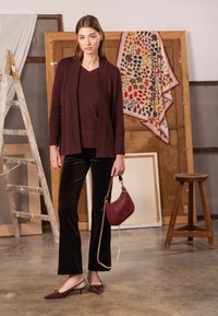 Bordowy kardigan nałożony na dopasowany top, zestawiony z czarnymi welurowymi spodniami. Dodatki to bordowa torebka i sandały na cienkich paskach z ostrym noskiem.