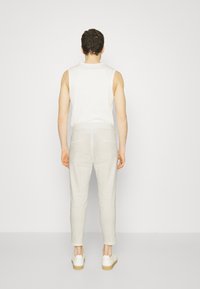 Férfi ujjatlan fehér felső, világosszürke, slim-fit nadrággal és fehér sportcipővel. Az öltözék kiadósan egyszerű és laza kialakítású.