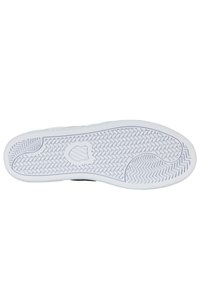 Musta sneakerin pohja valkoisesta kumimateriaalista; ominaisuuksina teksturoitu pito, aaltoilumuotoilu ja logo keskellä.