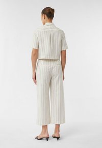 Cropped button-up shirt and wide-leg pants set in cream with black vertical stripes and tailored silhouette, featuring a back pleat detail.