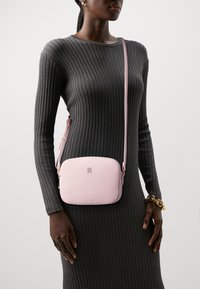 Borsa a tracolla rosa con una texture in pelle liscia, hardware dorato, forma rettangolare e tracolla regolabile, abbinata a un vestito grigio a coste.