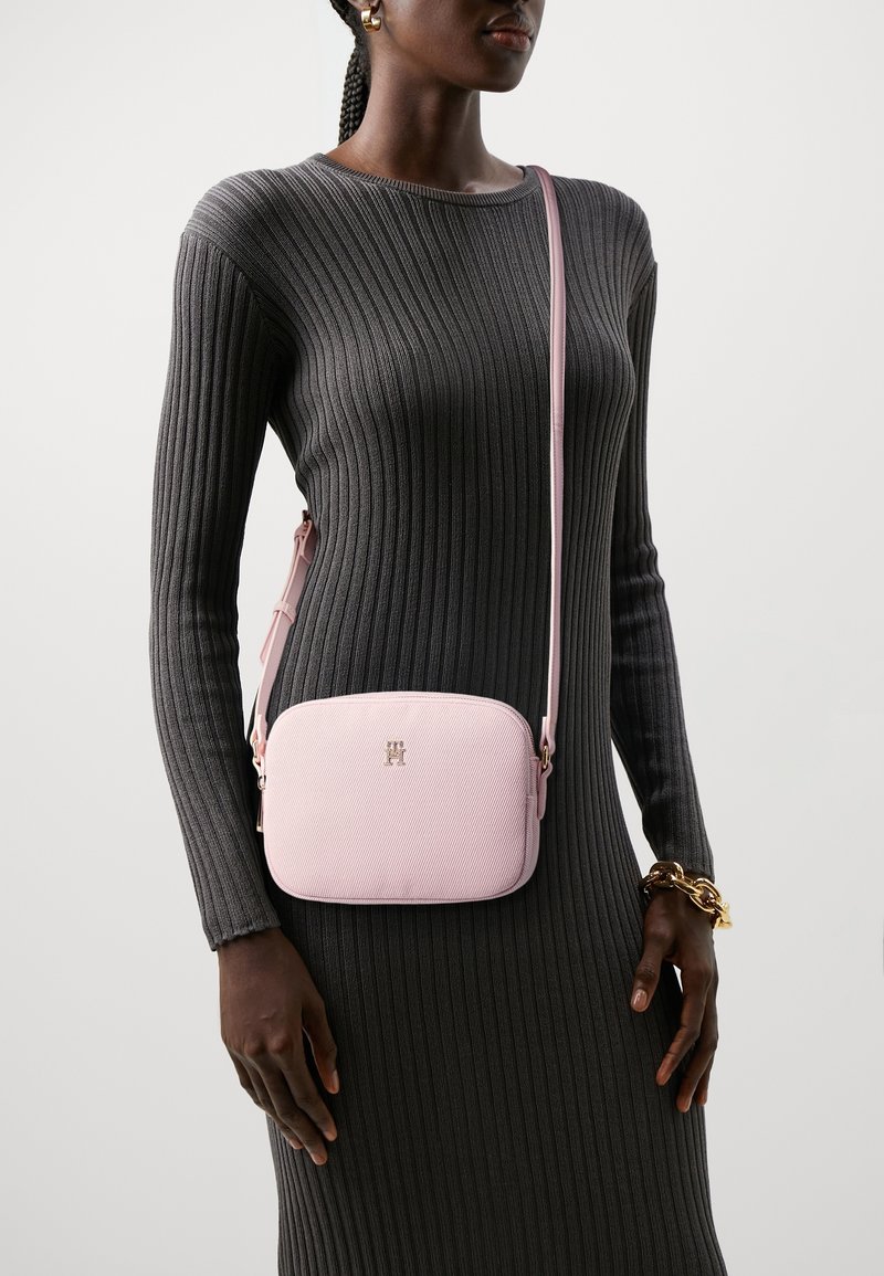 Borsa a tracolla rosa con una texture in pelle liscia, hardware dorato, forma rettangolare e tracolla regolabile, abbinata a un vestito grigio a coste.