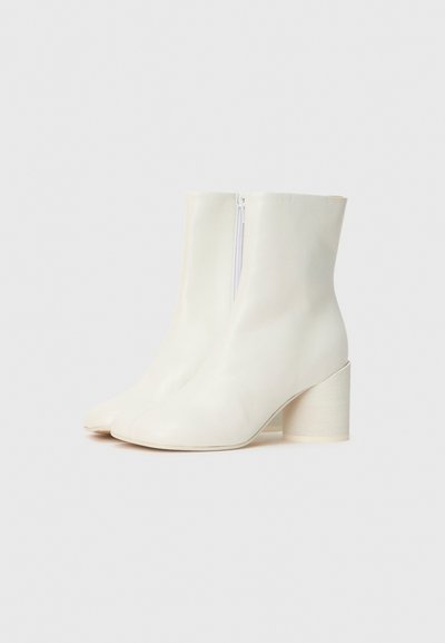 Bottines blanches en cuir lisse, dotées d'une fermeture éclair sur le côté et d'un large talon en bois. L'embout est légèrement pointu pour un look chic.