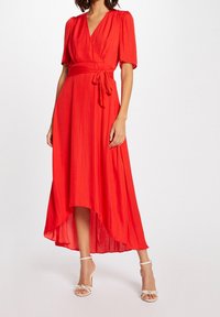 Rode wikkeljurk met korte pofmouwen, een strik taille en een asymmetrische zoom. Gemaakt van lichte stof met een gladde textuur.