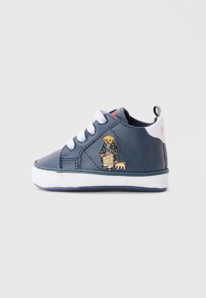 Tengerészkék bőr sneaker fehér fűzővel, kontrasztos varrással, és hímzett plüssmackó és kutya mintával az oldalon. Fehér talp.