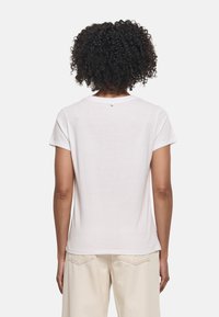 T-shirt en coton blanc à manches courtes et col rond, avec un petit logo au dos. Texture lisse et coupe décontractée.