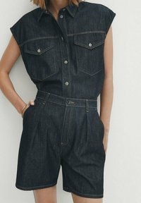 Chemise sans manches en denim foncé avec deux poches poitrine, boutonnière à l'avant, et shorts taille haute plissés, avec des coutures contrastées et une coupe ajustée.