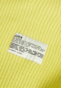 Étiquette de vêtement sur un tissu tricoté jaune avec un texte motivant célébrant les jeunes femmes et listant des adjectifs valorisants.