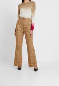 Bruna rutiga vida byxor med bälte i midjan, tillsammans med en ombre stickad tröja som övergår från beige till rosa. Svarta spetsiga klackar.