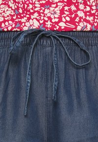 Shorts en denim bleu avec une taille élastique et un cordon de serrage, présentant une texture lisse et un design décontracté. Haut à imprimé floral au-dessus.