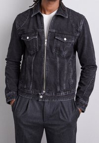 Svart denimjacka med dragkedja framtill, två bröstfickor och spetsig krage. Har vit sömnad, sidfickor och en figursydd design.