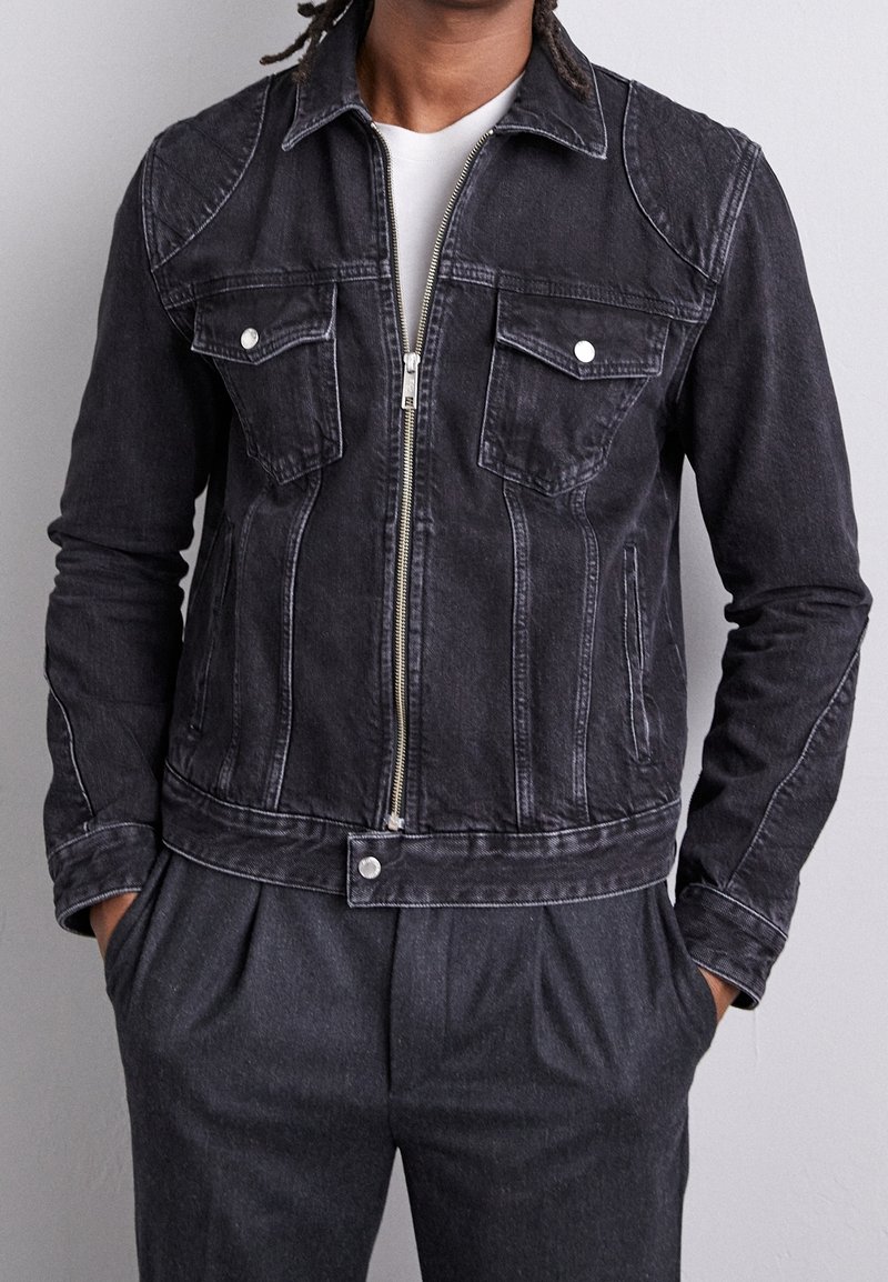 Svart denimjacka med dragkedja framtill, två bröstfickor och spetsig krage. Har vit sömnad, sidfickor och en figursydd design.