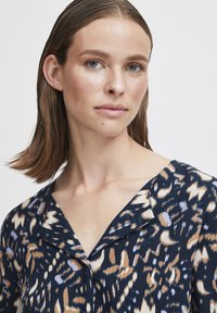 Blusa blu navy con scollatura a V, caratterizzata da una stampa astratta testurizzata in crema, beige e blu, messa in risalto da una vestibilità rilassata e da un tessuto morbido.