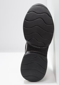 Semelle de chaussure noire avec des motifs de bande de roulement ondulés et le texte embossé "KARL LAGERFELD" sur la partie de la voûte plantaire, sur un fond blanc.