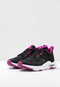 Un paio di scarpe da ginnastica nere e viola con suole bianche, tomaia in rete e ammortizzazione ad aria visibile su una superficie bianca contro uno sfondo semplice.