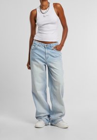 Vitt linne med svart logotyp, kombinerat med ljusblå, löst sittande jeans i denim med en blekt textur och detaljerade fickor framtill.