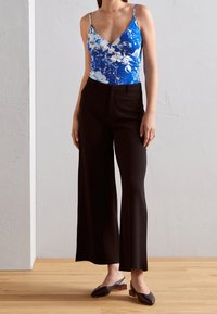 Blue floral bodysuit with a deep V-neck and thin straps, paired with high-waisted black wide-leg trousers and black slingback shoes.