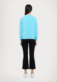 Sudadera de tejido suave en azul claro, con cuello redondo y puños acanalados, combinada con pantalones negros de campana y zapatillas blancas.