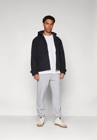 Casaco preto com capuz, t-shirt branca e calças de treino cinzentas. Ténis com sola castanha clara. Design simples, corte descontraído. Textura suave do tecido.